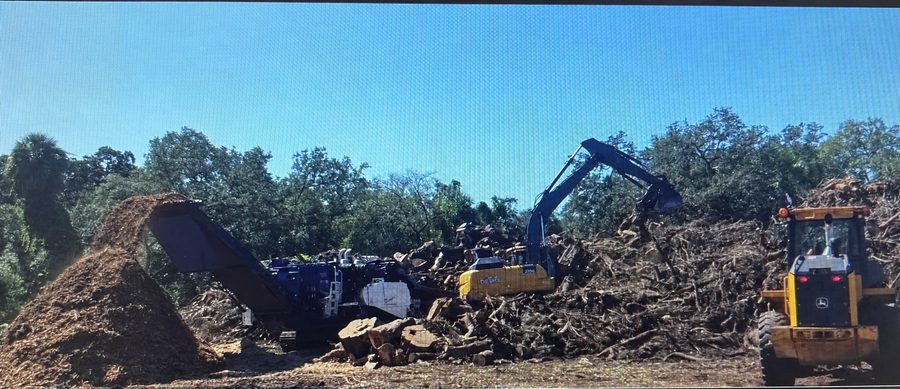 Wood grinder and excavator processing branches beside a mulch pile